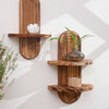 Two wooden wall shelves with natural grain holding a white flower and a small glass vase.