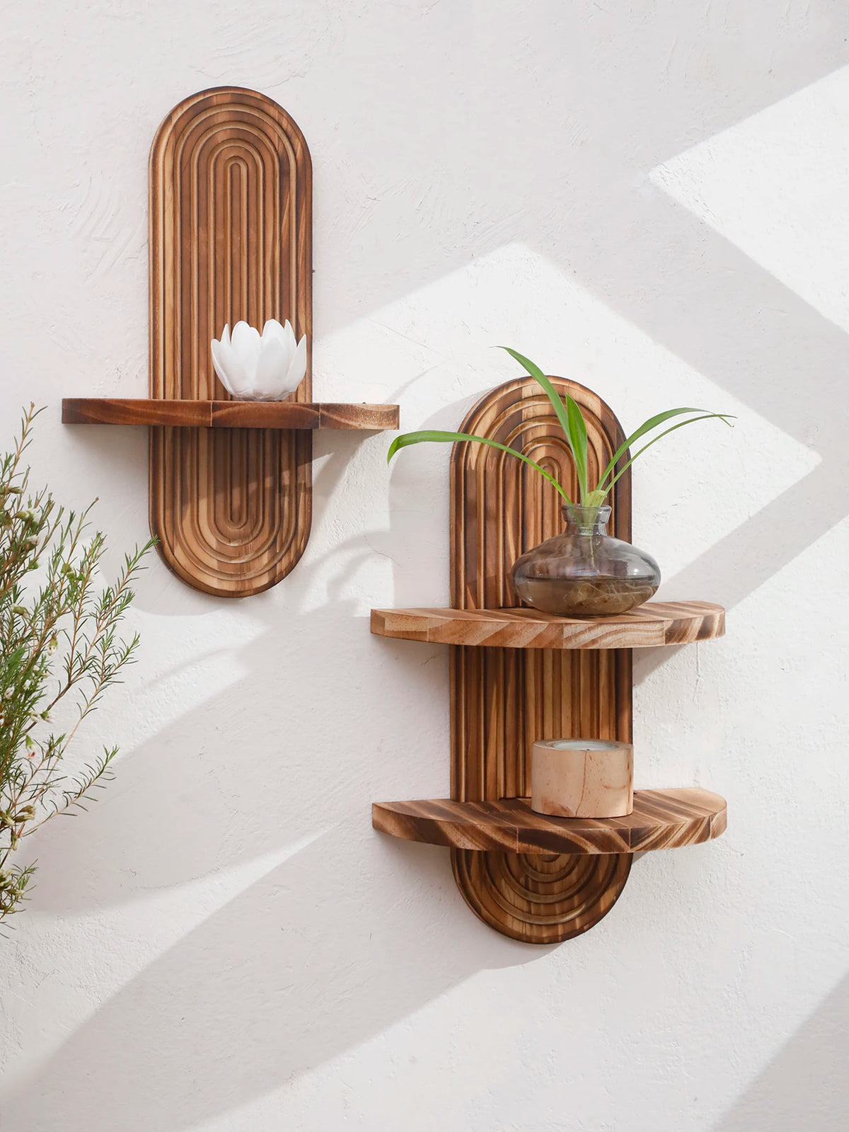 Two wooden wall shelves with natural grain holding a white flower and a small glass vase.
