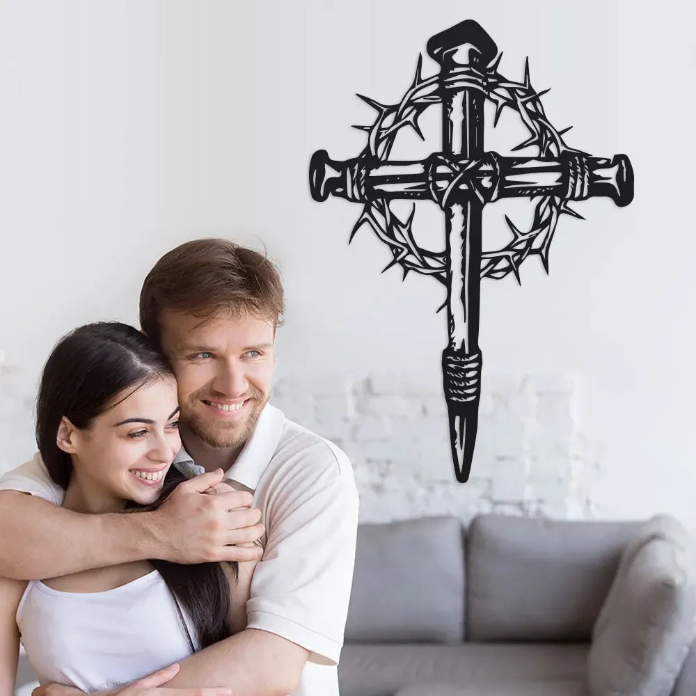 A couple smiling while looking at a black metal cross wall art with thorn details.
