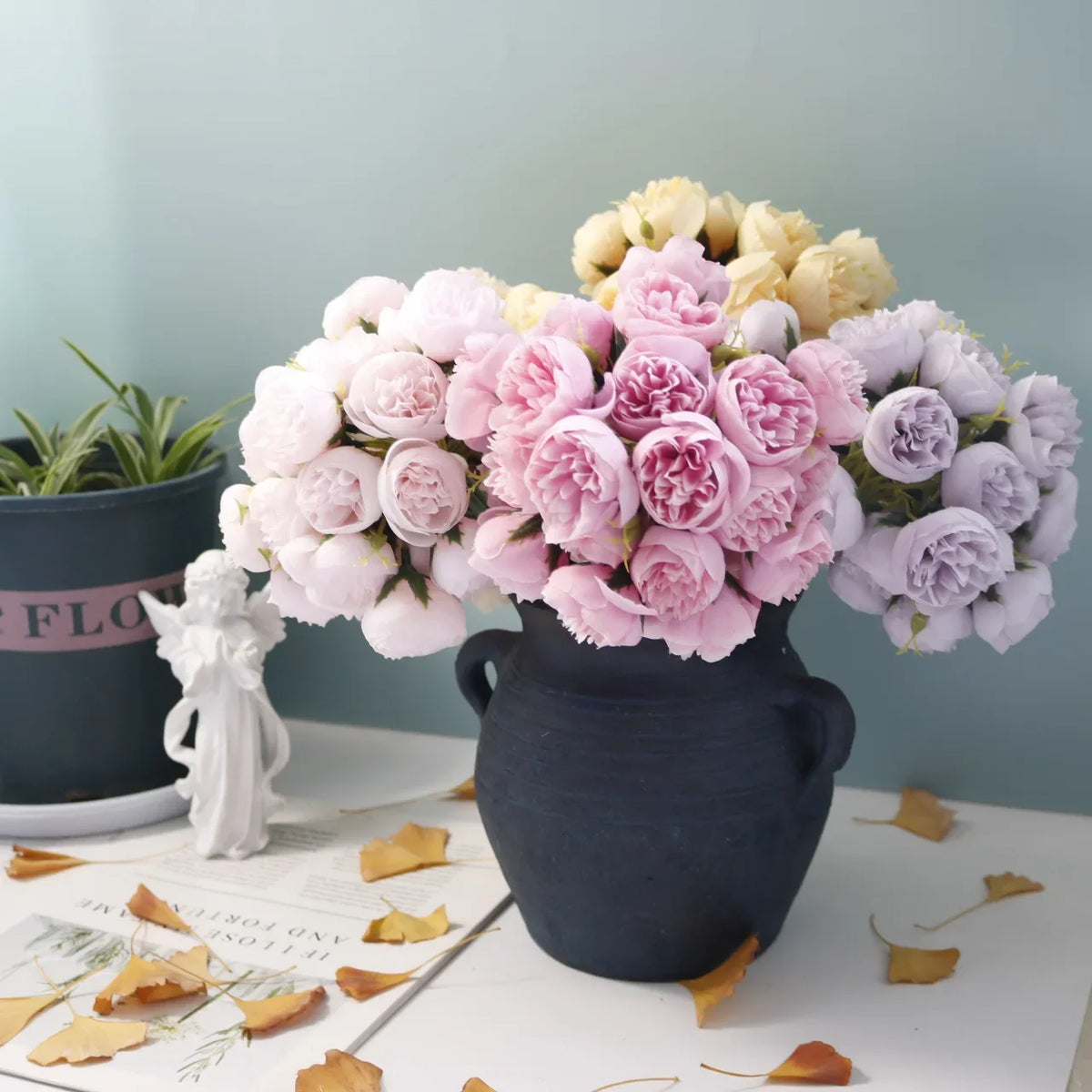 A bouquet of artificial pink peony silk flowers in a dark vase on a white surface.