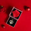 A pink velvet box containing a red rose and a gold heart pendant necklace on a red background.