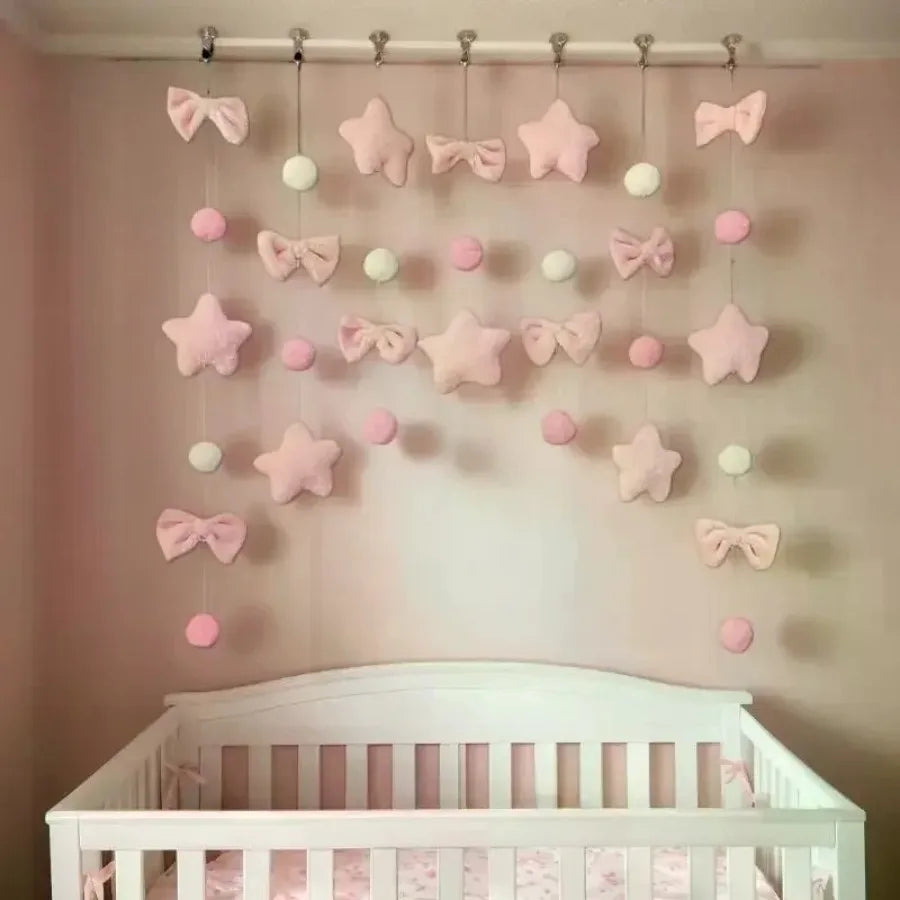 Pink tassel door curtain decorated with heart and star shapes hanging on a wall above a crib
