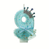 A light blue glitter candle decoration shaped like the number 8 with a silver crown and a sheer blue mesh skirt.