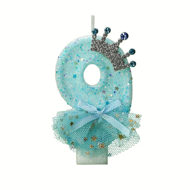 A light blue glitter candle decoration shaped like the number 8 with a silver crown and a sheer blue mesh skirt.