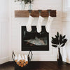 Three white knitted socks are hanging from a wooden rack above a black fireplace mantel.