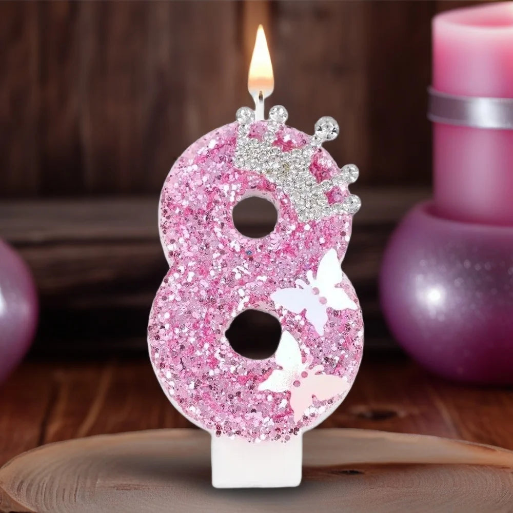 A pink glitter number eight candle with a crown and butterfly design set against a blurred background of candles.