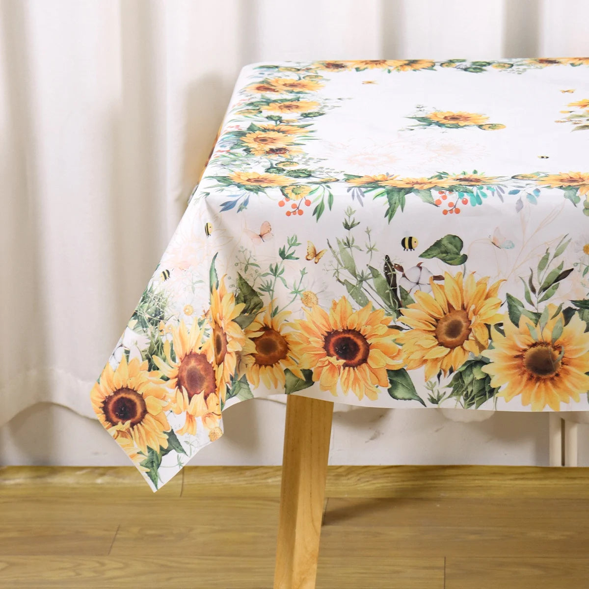 A white tablecloth with a yellow and green sunflower print displayed on a wooden table.