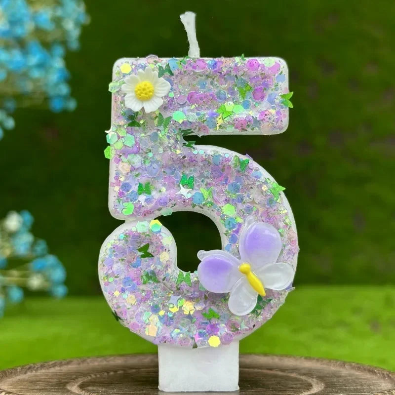 A handmade number cake candle shaped like the number 5 decorated with purple glitter, a white flower, and a lavender butterfl