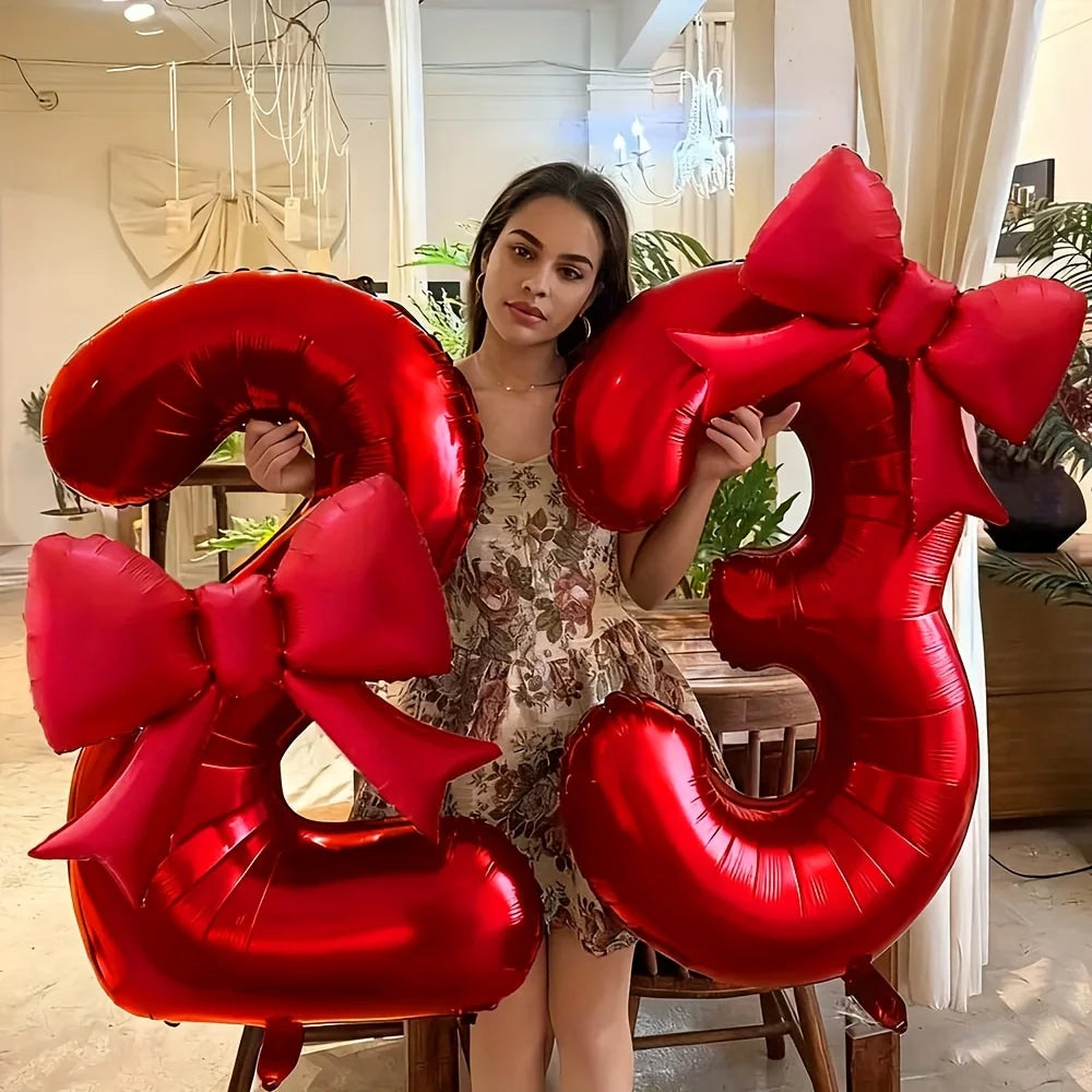A woman holds large red foil number balloons shaped like the number 32 with matching bows.