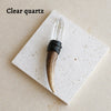 A clear quartz scepter wand with a wooden handle and black cord wrapped around it, displayed on a white square card.