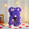 Lila künstlicher Rosen-Teddybär mit Lichterketten, auf weißer Fläche.