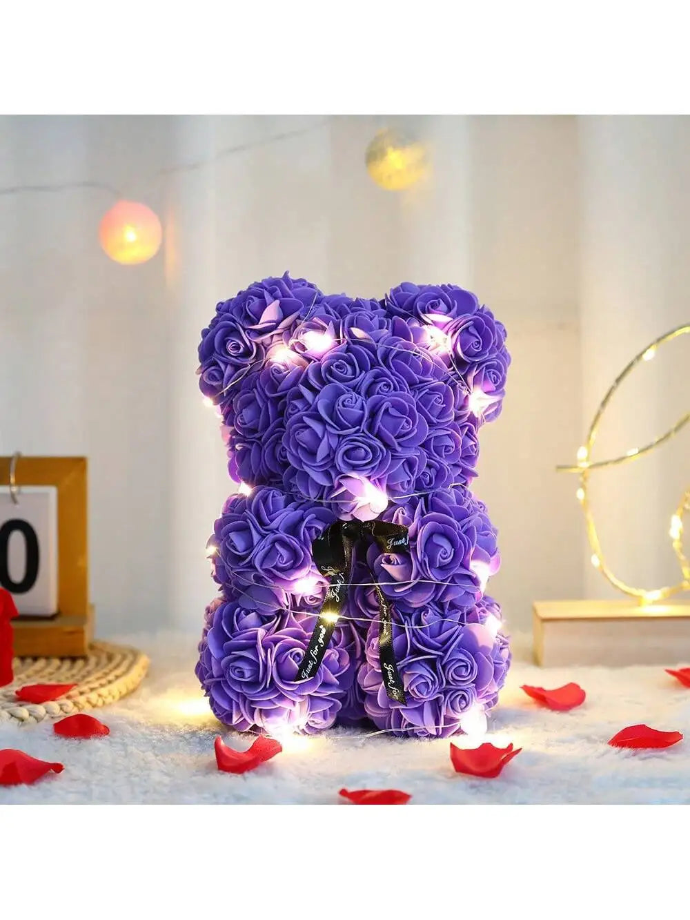 Lila künstlicher Rosen-Teddybär mit Lichterketten, auf weißer Fläche.