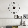 A black and gold frameless acrylic digital wall clock with Roman numerals on a white wall.