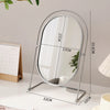 A silver oval vanity mirror with a rotating frame and a stand is shown on a white surface.