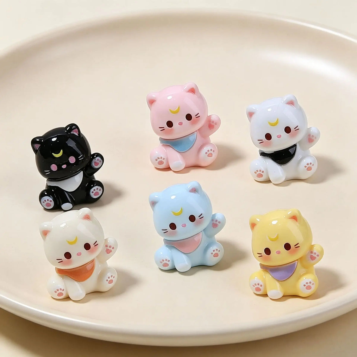 A collection of colorful, cute 3D resin cat animal keychains displayed on a light pink plate.
