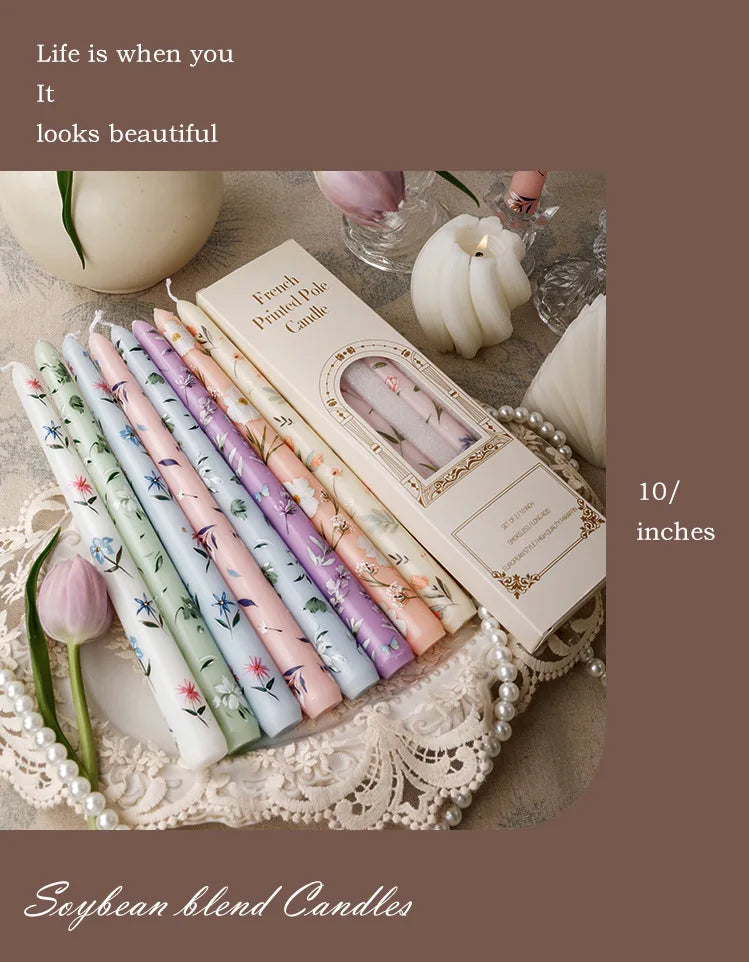 A collection of pink and green scented soy blend candles in long sticks displayed on a lace fabric with white pearls.