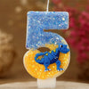 A birthday candle shaped like the number 5, featuring blue glitter and a small blue dinosaur on an orange base.