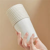 A hand is holding a white, ribbed disposable paper cup against a neutral background.