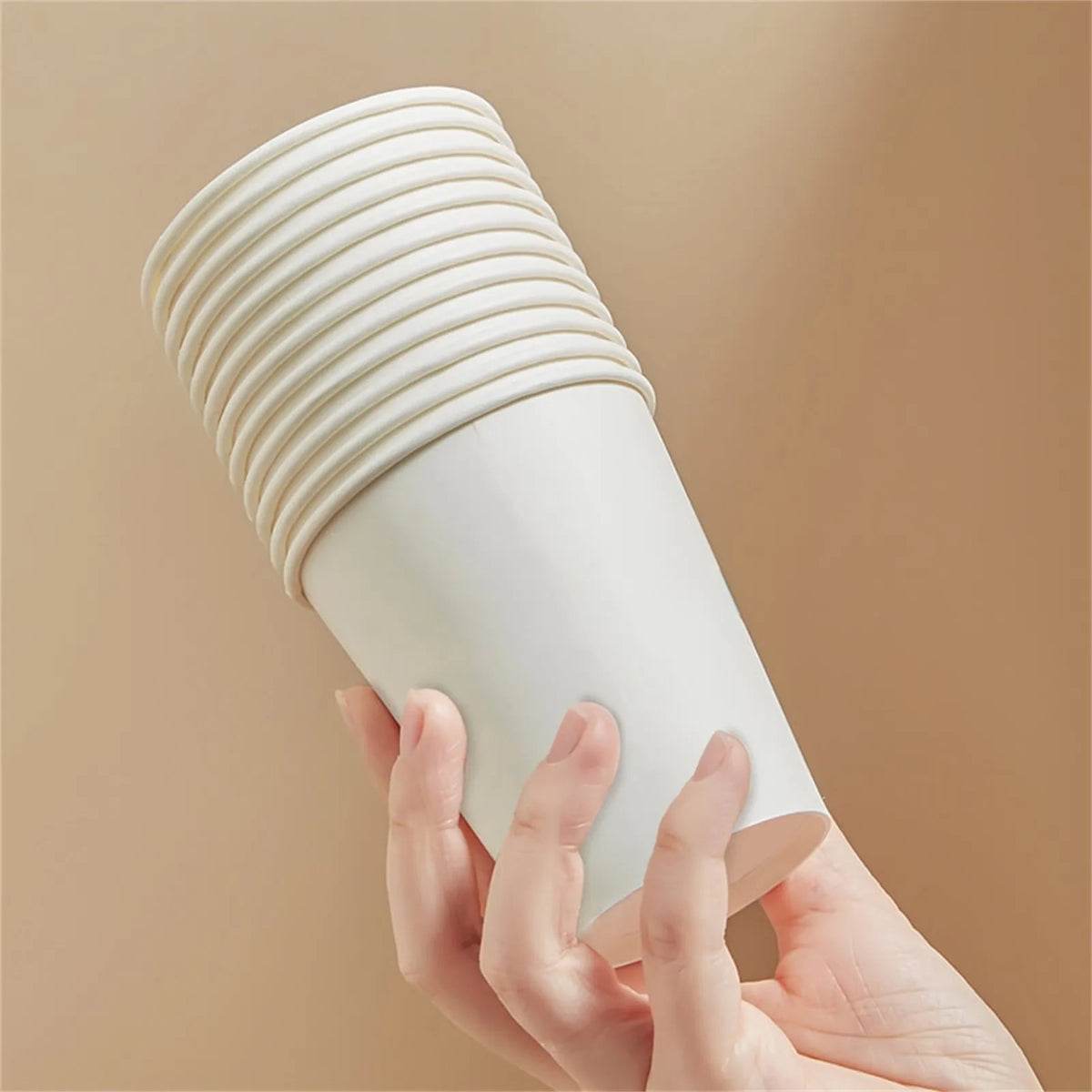 A hand is holding a white, ribbed disposable paper cup against a neutral background.