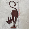 A silhouette of a cat with a curled tail is cut into a piece of dark brown metal.