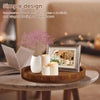 A handcrafted wooden serving tray holds white candles and a small floral arrangement in a warm indoor setting.
