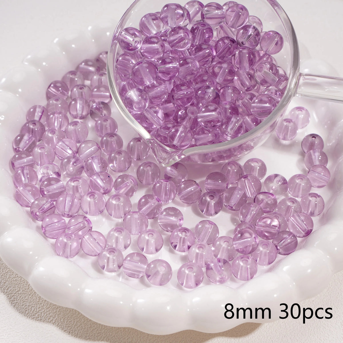 A clear glass jar filled with purple round spacer beads for jewelry making, displayed on a white dish.