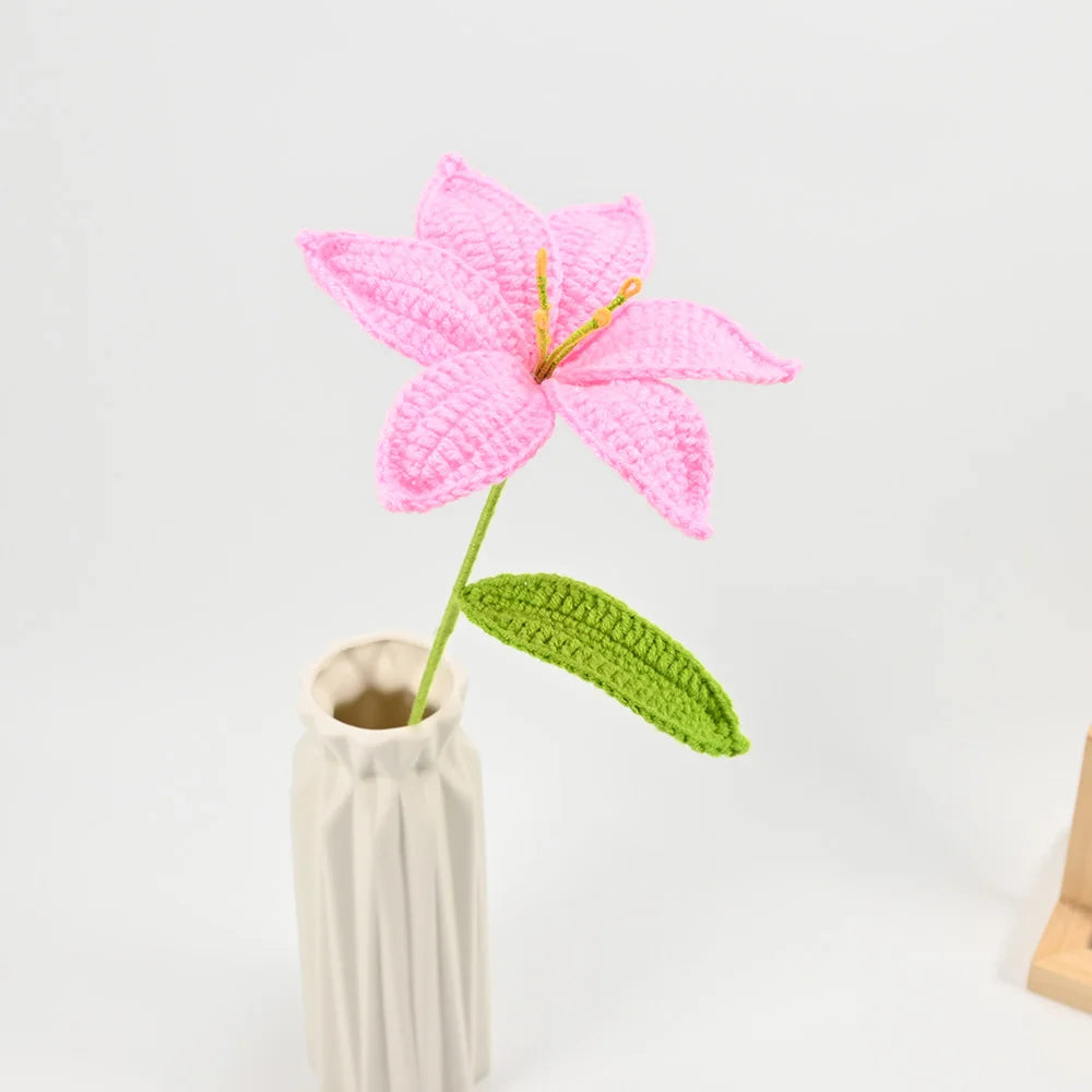Hand-crocheted pink lily flower with a green stem displayed in a beige vase.