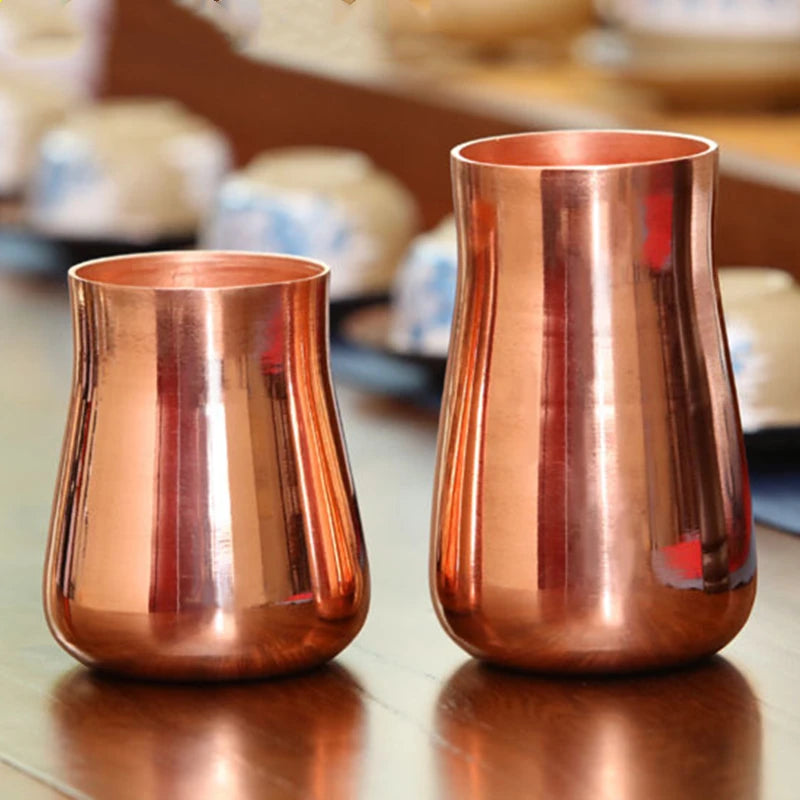 A handcrafted pure copper vintage mug with a tapered shape is shown on a wooden surface.