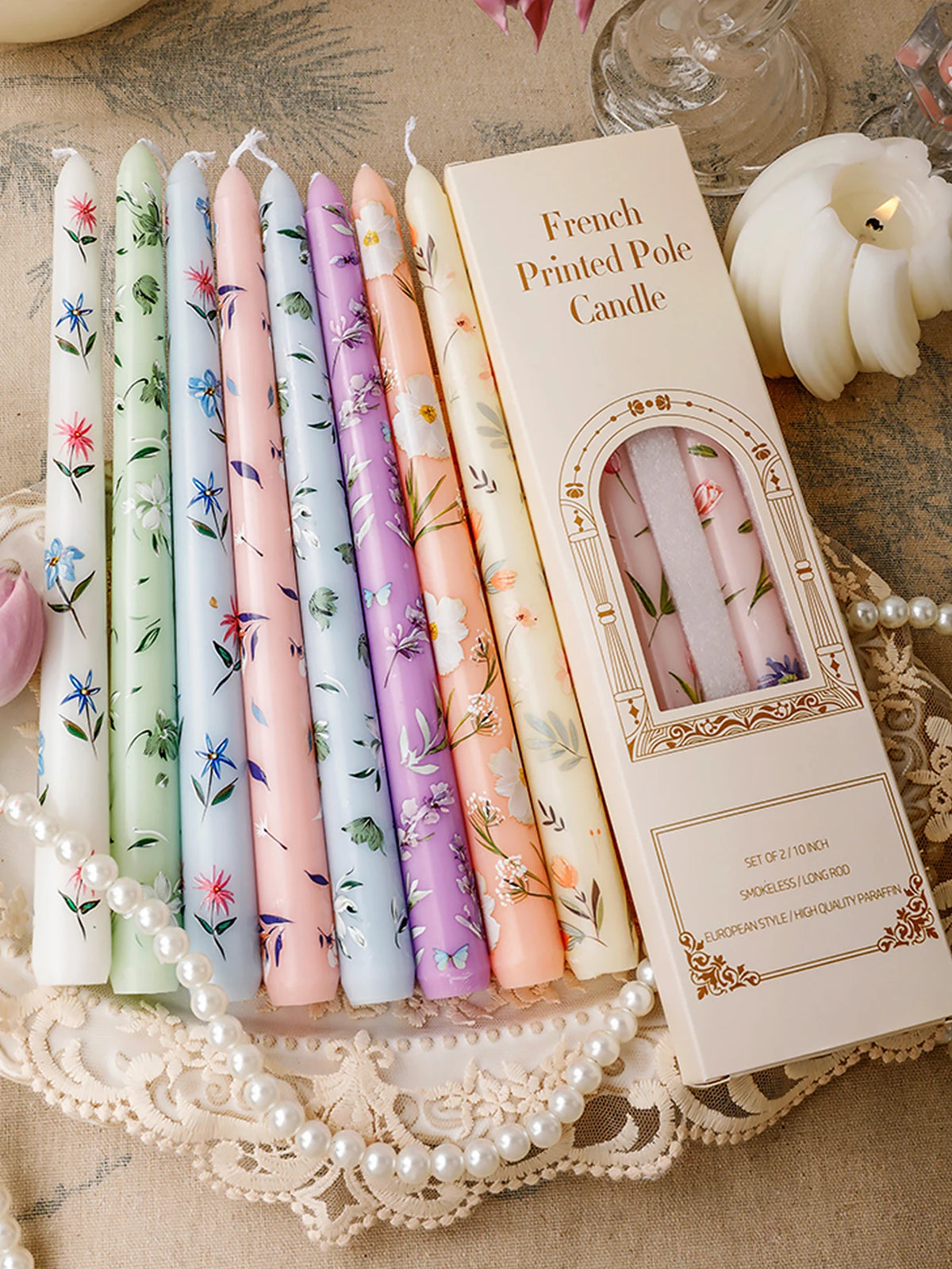 A set of French printed long stick candles in various pastel colors displayed on a lace cloth.