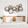 A set of four hexagonal wooden floating shelves displaying decorative items above a bed.