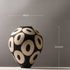 A black ceramic vase with a geometric pattern of light beige circles, shown against a gray background.