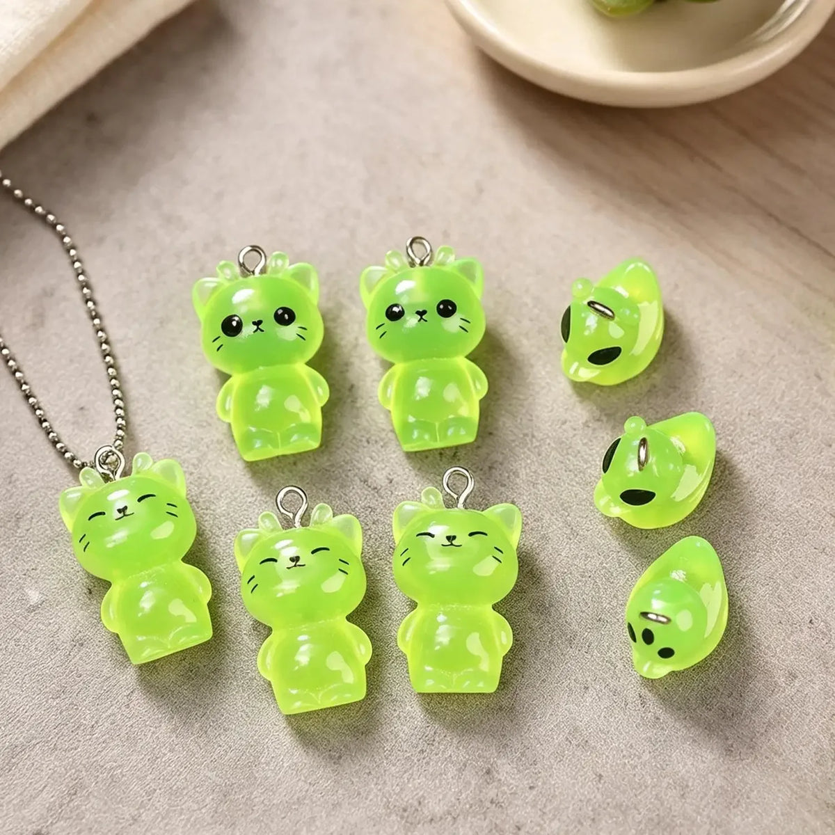 A collection of glow-in-the-dark resin charms shaped like cats and ducks are displayed on a light surface.
