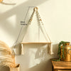 A macrame wood floating wall shelf with a hanging rope is displayed against a light wall, casting a shadow.