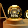 A clear glass crystal ball with a laser engraved design of a Ferris wheel resting on a wooden base.
