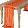Orange semi-sheer gauze table runner draped over a wooden table.