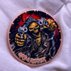 A copper challenge coin featuring a grim reaper design with a skull and guns.