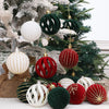 A collection of velvet Christmas tree hanging ornaments in shades of green, red, and white are displayed on a snowy evergreen