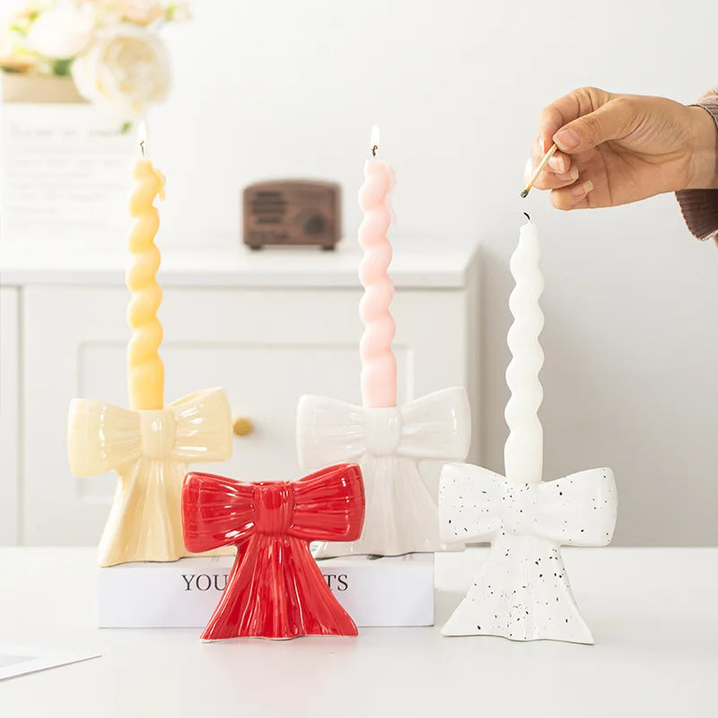 A hand is lighting a white ceramic bow candle holder with a thin candle.