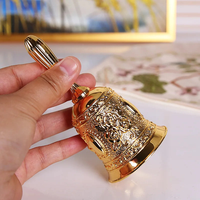 A hand holds an ornate brass hand call bell with detailed floral patterns.