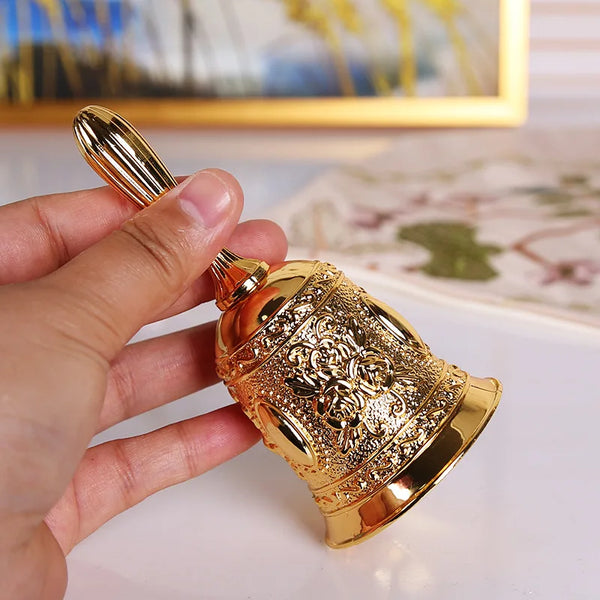 A hand holds an ornate brass hand call bell with detailed floral patterns.