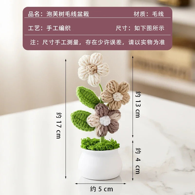 A hand-woven crochet flower in a white pot, featuring green leaves and a central flower.