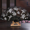 Black lace folding fan decorated with white roses and gold accents on a wooden stand