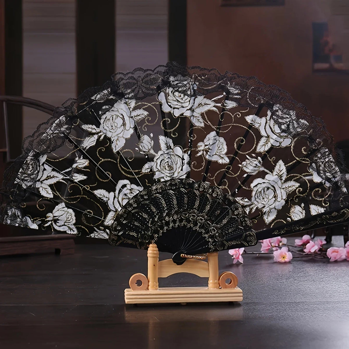 Black lace folding fan decorated with white roses and gold accents on a wooden stand