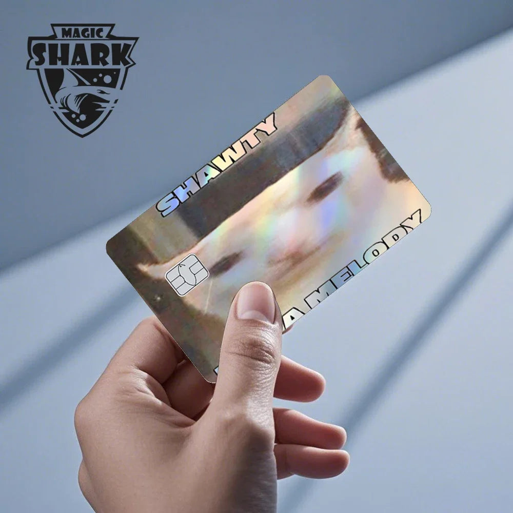 A hand holds a holographic credit card skin sticker with the words SHAWTY and MELODY printed on it.