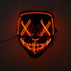 A glowing orange LED mask shaped like a menacing face with crossed eyes and a wide grin, mounted on a dark wall.