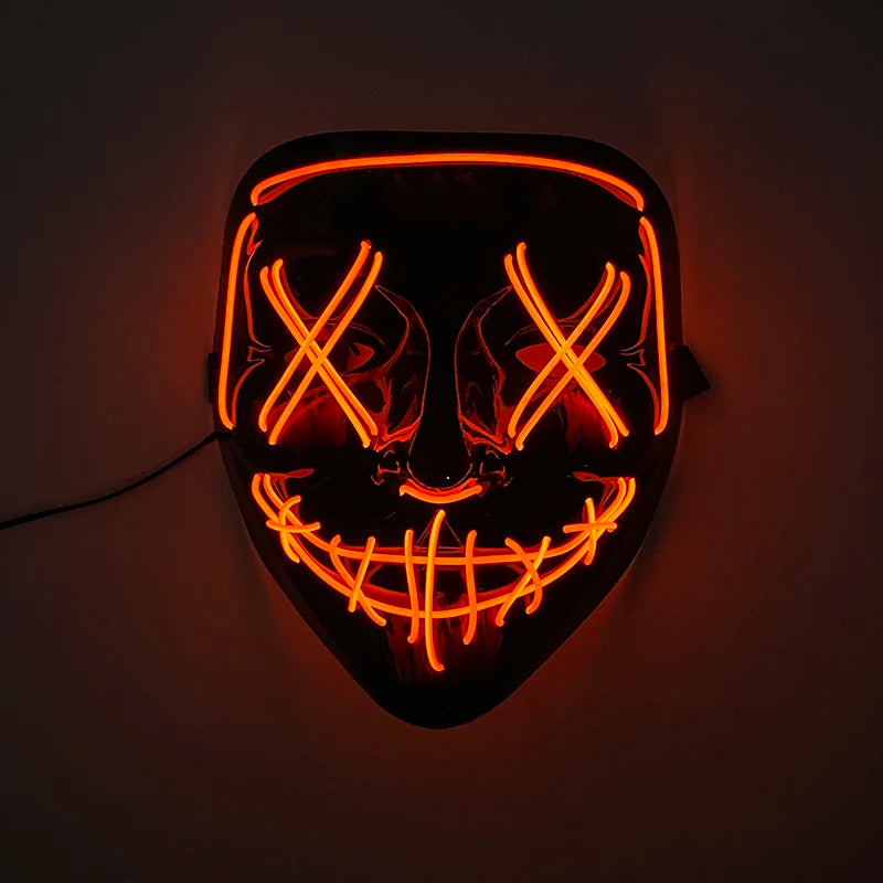 A glowing orange LED mask shaped like a menacing face with crossed eyes and a wide grin, mounted on a dark wall.