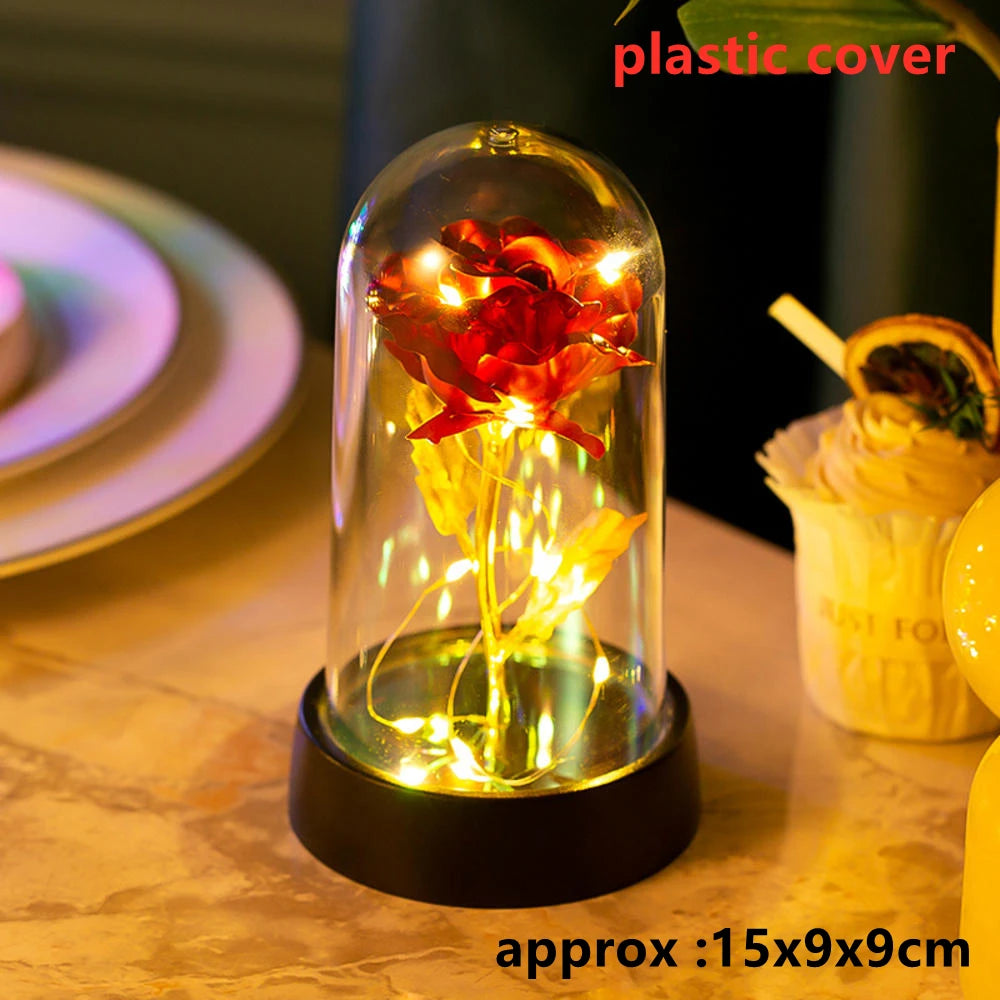 An LED galaxy rose artificial flower displayed inside a glass dome on a dark surface.