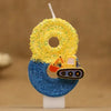 A birthday cake candle shaped like a construction excavator, featuring yellow glitter and blue glitter on a white stick.