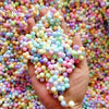 A hand holds a pile of colorful pastel foam beads for crafting and decoration.