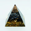 A clear pyramid-shaped crystal containing dark stones and a coiled copper wire, used for Reiki and meditation.